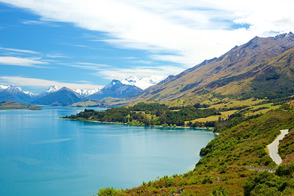 Lake Wakatipu shoreline with the road running alongside it on a beautiful sunny day.
