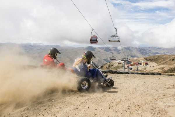 Two visitors enjoying carting down the sunny, sandy mountain under the gondolas.
