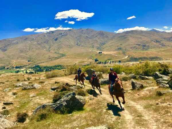 Three horse riders at speed with an epic mountain backdrop.